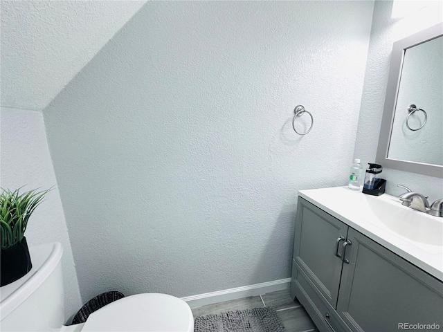 bathroom featuring baseboards, toilet, vanity, and a textured wall