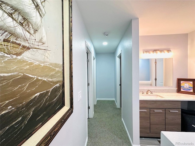 hallway featuring light colored carpet, baseboards, and a sink