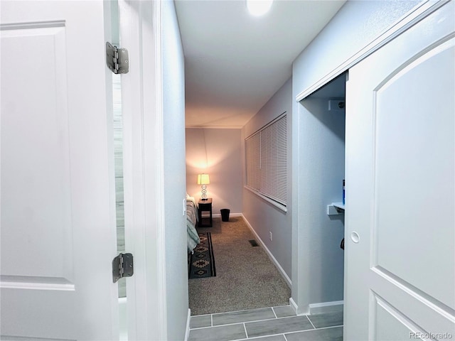 hallway featuring baseboards, tile patterned floors, and carpet