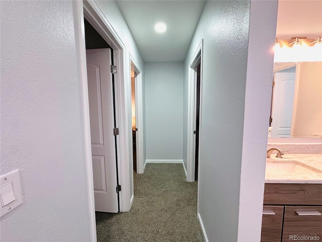 hall featuring carpet, baseboards, and a sink