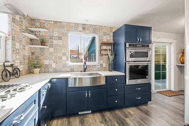 kitchen featuring hardwood / wood-style flooring, stainless steel double oven, blue cabinets, and sink