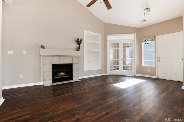 unfurnished living room featuring built in features, lofted ceiling, a tiled fireplace, dark wood-type flooring, and french doors