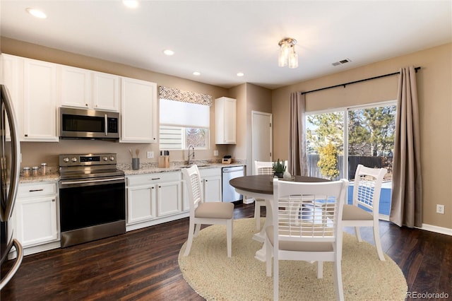 kitchen featuring appliances with stainless steel finishes, dark hardwood / wood-style floors, sink, white cabinets, and light stone countertops