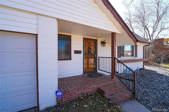 view of exterior entry with brick siding, an attached garage, and a porch