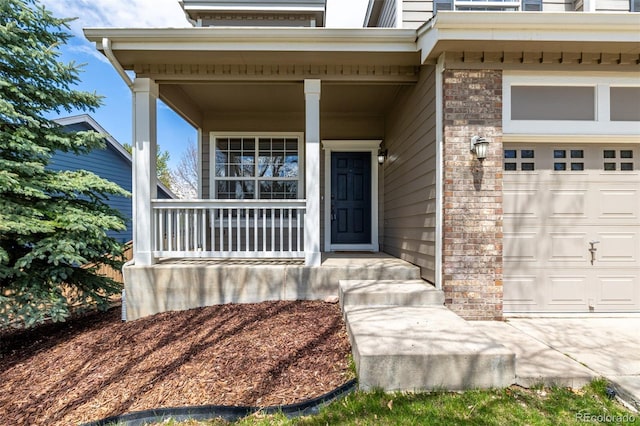 doorway to property with an attached garage, a porch, and brick siding