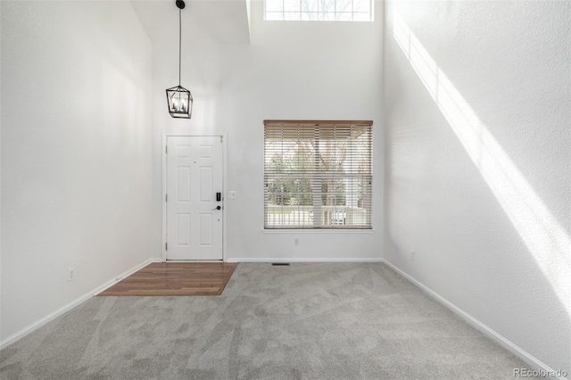 carpeted foyer entrance with a high ceiling, a chandelier, and baseboards