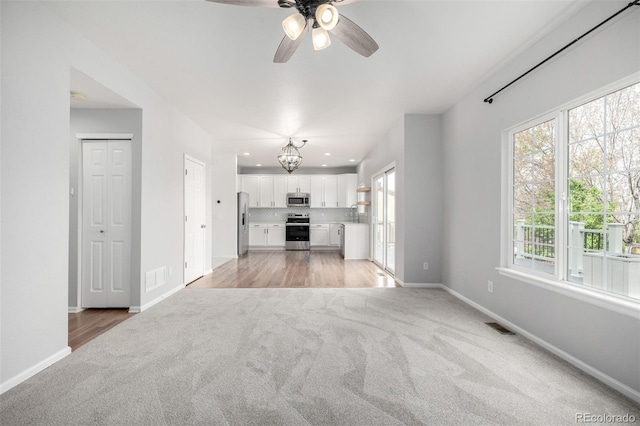 unfurnished living room featuring light colored carpet, baseboards, ceiling fan with notable chandelier, and visible vents
