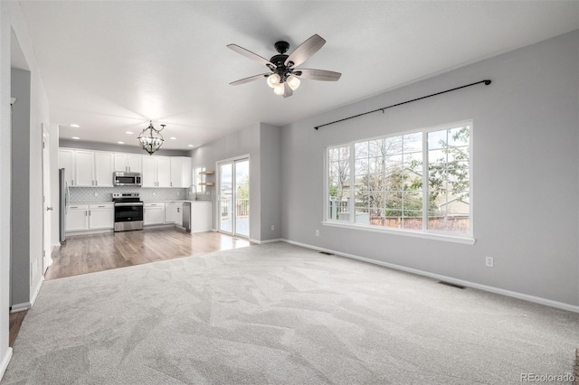 unfurnished living room featuring plenty of natural light, baseboards, ceiling fan with notable chandelier, and light carpet