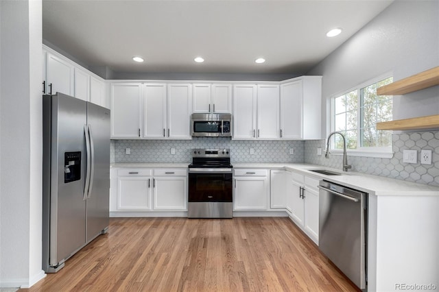 kitchen featuring appliances with stainless steel finishes, a sink, light countertops, white cabinets, and light wood finished floors