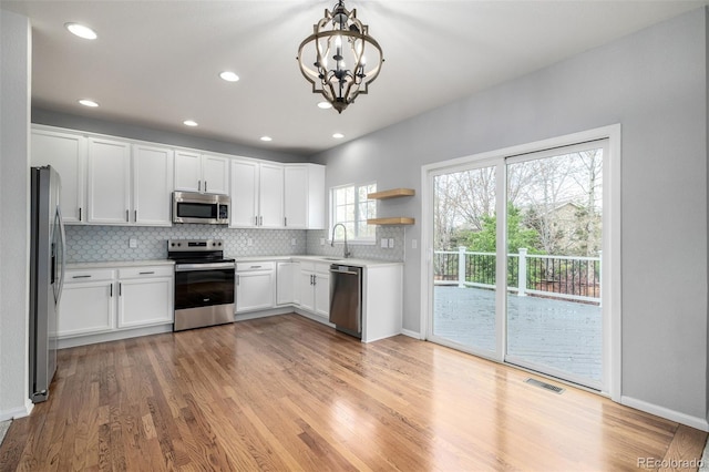 kitchen featuring open shelves, a notable chandelier, appliances with stainless steel finishes, light countertops, and decorative backsplash