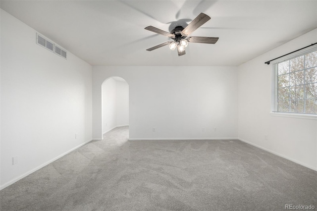 carpeted empty room with visible vents, arched walkways, baseboards, and a ceiling fan