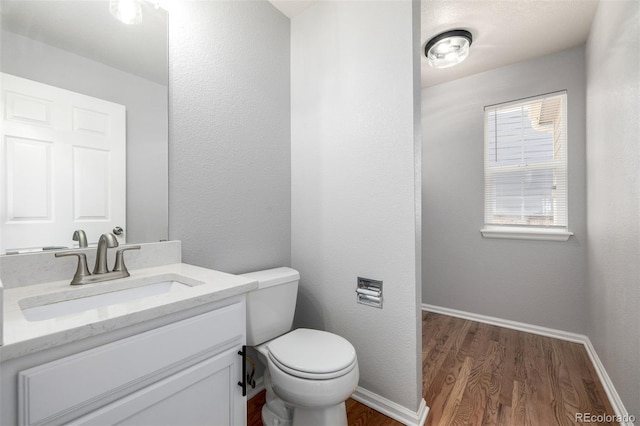 half bathroom with toilet, baseboards, wood finished floors, and vanity