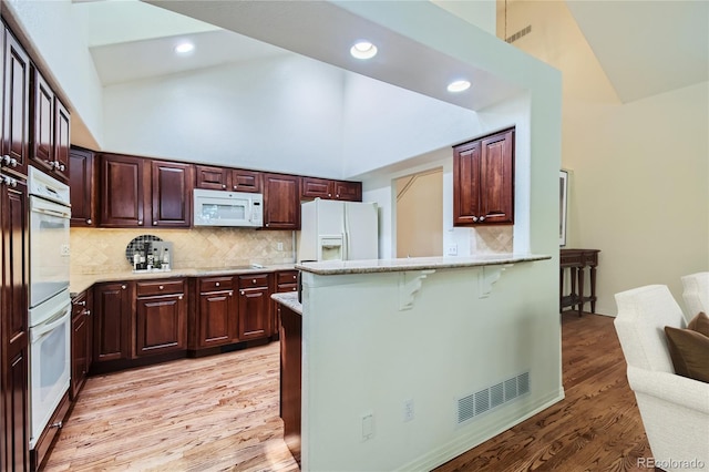 kitchen featuring tasteful backsplash, light hardwood / wood-style flooring, high vaulted ceiling, white appliances, and a kitchen bar