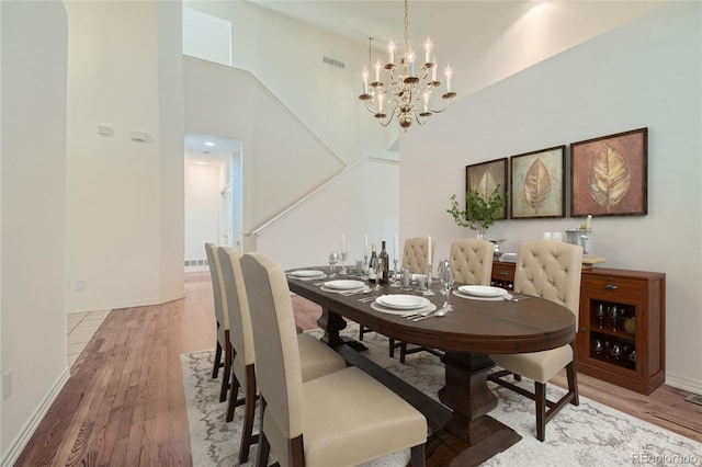 dining room featuring a chandelier, a towering ceiling, and light wood-type flooring