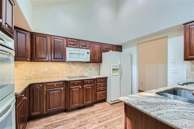 kitchen with decorative backsplash, light stone countertops, light wood-type flooring, white appliances, and sink