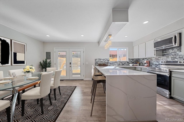 kitchen with french doors, light hardwood / wood-style flooring, decorative backsplash, light stone countertops, and stainless steel appliances