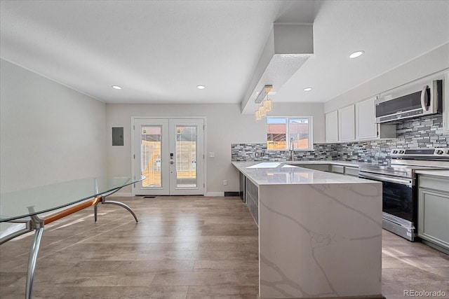 kitchen featuring french doors, light stone counters, stainless steel appliances, light hardwood / wood-style floors, and white cabinetry