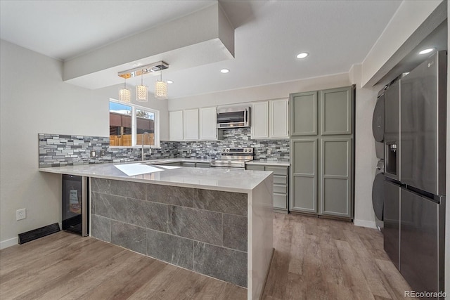 kitchen featuring kitchen peninsula, appliances with stainless steel finishes, light wood-type flooring, white cabinetry, and hanging light fixtures