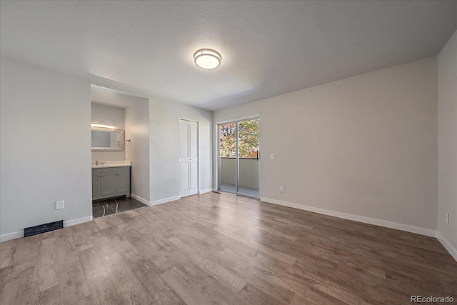 unfurnished bedroom with hardwood / wood-style floors, sink, a textured ceiling, connected bathroom, and a closet