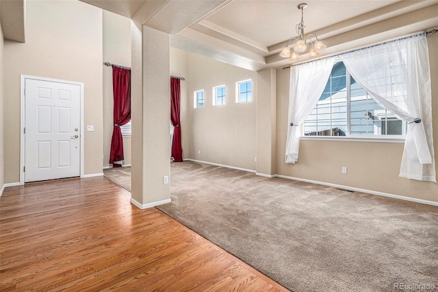 interior space featuring carpet floors, a raised ceiling, an inviting chandelier, wood finished floors, and baseboards