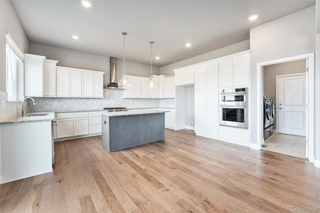 7293 Xenophon Ct, Arvada, CO 80004 - kitchen featuring wall chimney exhaust hood, washer and clothes dryer, stainless steel double oven, a center island, and decorative backsplash