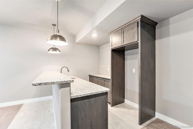 7293 Xenophon Ct, Arvada, CO 80004 - kitchen featuring light stone counters, pendant lighting, tasteful backsplash, and dark brown cabinetry