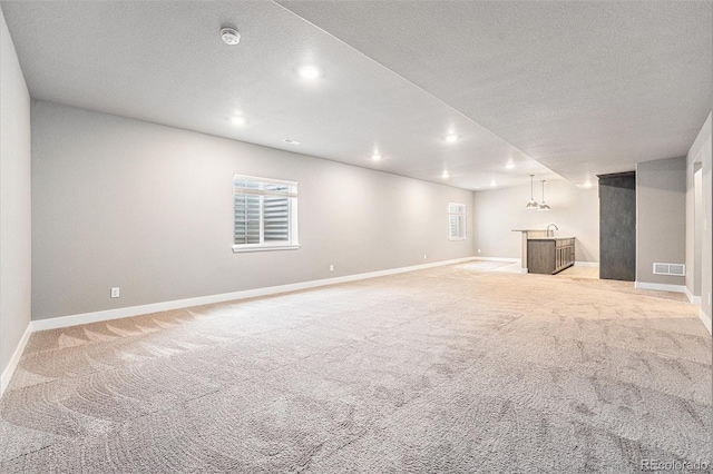 7293 Xenophon Ct, Arvada, CO 80004 - unfurnished living room with bar with sink, light colored carpet, recessed lighting, and a textured ceiling