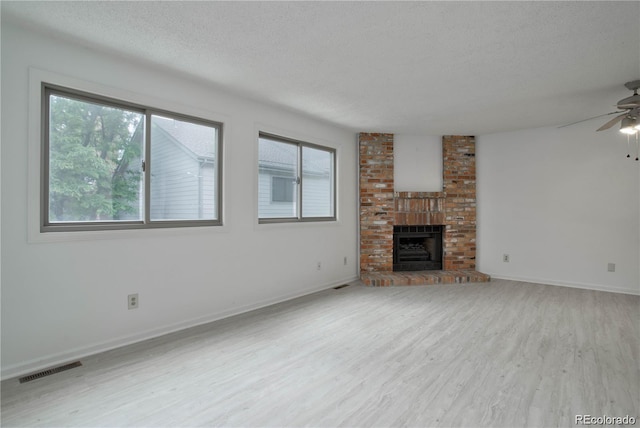 unfurnished living room with ceiling fan, light hardwood / wood-style flooring, a brick fireplace, and a textured ceiling