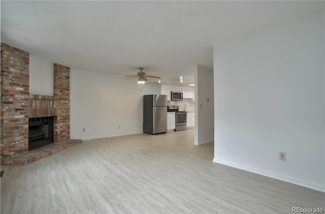 unfurnished living room with ceiling fan, a fireplace, light hardwood / wood-style floors, and a textured ceiling