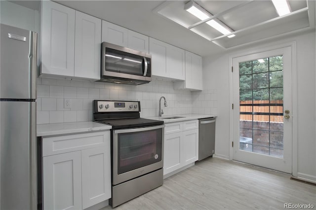 kitchen with sink, light hardwood / wood-style flooring, stainless steel appliances, decorative backsplash, and white cabinets