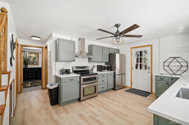 kitchen with light hardwood / wood-style flooring, wall chimney range hood, tasteful backsplash, appliances with stainless steel finishes, and ceiling fan