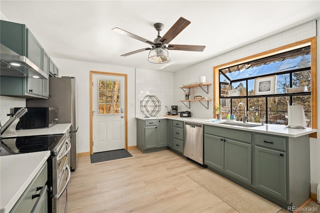 kitchen with stainless steel appliances, sink, green cabinetry, ceiling fan, and light hardwood / wood-style floors