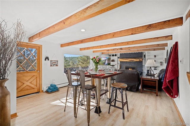 dining area featuring a fireplace, light hardwood / wood-style floors, and beamed ceiling