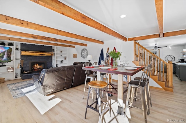 dining room with light hardwood / wood-style floors, beamed ceiling, ceiling fan, a fireplace, and built in shelves