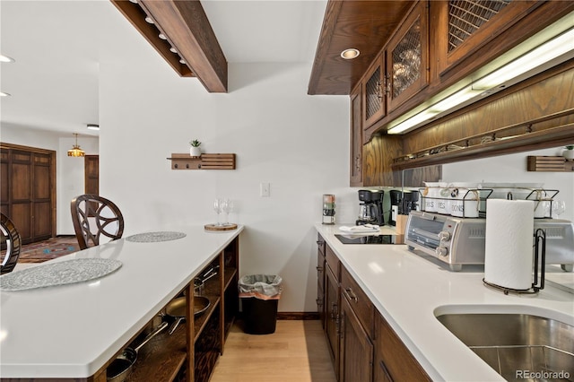 kitchen featuring light wood-type flooring, black electric stovetop, beam ceiling, decorative light fixtures, and sink