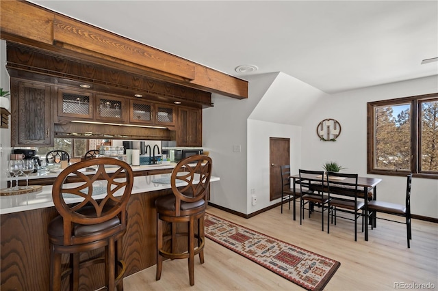 kitchen with a breakfast bar, light hardwood / wood-style flooring, beamed ceiling, and dark brown cabinetry