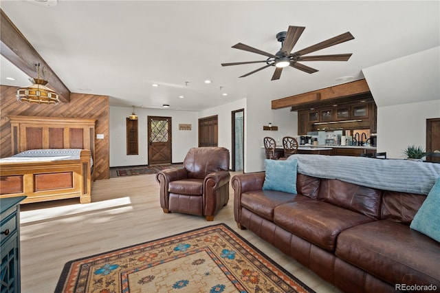 living room with light hardwood / wood-style floors, ceiling fan, and wooden walls