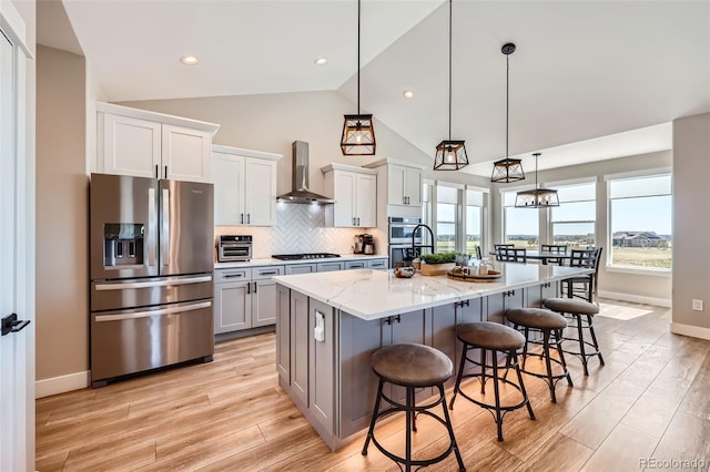 229 High Meadows Loop, Elizabeth, CO 80107 - kitchen featuring appliances with stainless steel finishes, wall chimney exhaust hood, light wood finished floors, a breakfast bar, and a large island with sink