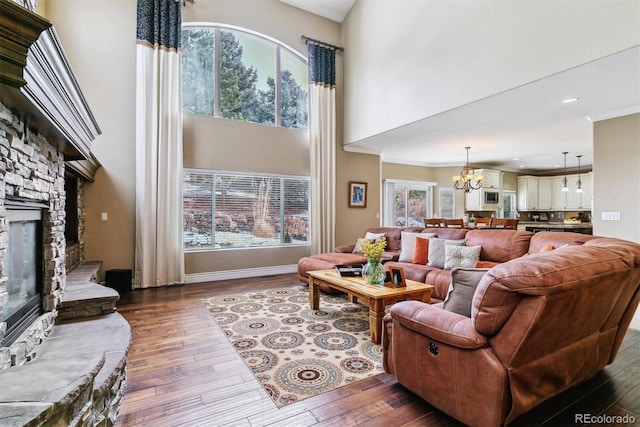 living room featuring a chandelier, a stone fireplace, a wealth of natural light, and wood-type flooring