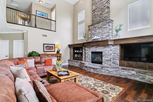 living room featuring a stone fireplace, wood-type flooring, ornamental molding, and a towering ceiling