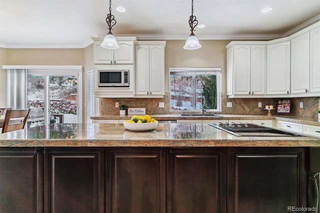 kitchen featuring a center island, stainless steel microwave, black electric stovetop, sink, and decorative light fixtures