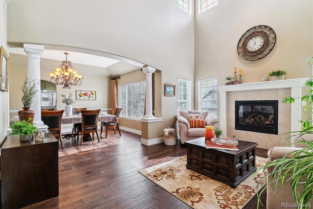 living room with decorative columns, wood-type flooring, a tile fireplace, and an inviting chandelier