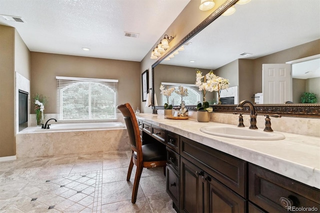 bathroom with a textured ceiling, tiled tub, and vanity