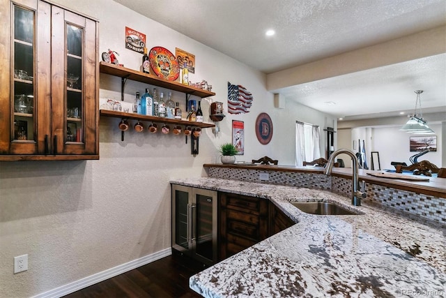 kitchen with light stone counters, sink, a textured ceiling, and beverage cooler