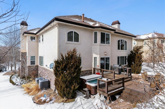 snow covered house featuring cooling unit, a deck, and a jacuzzi