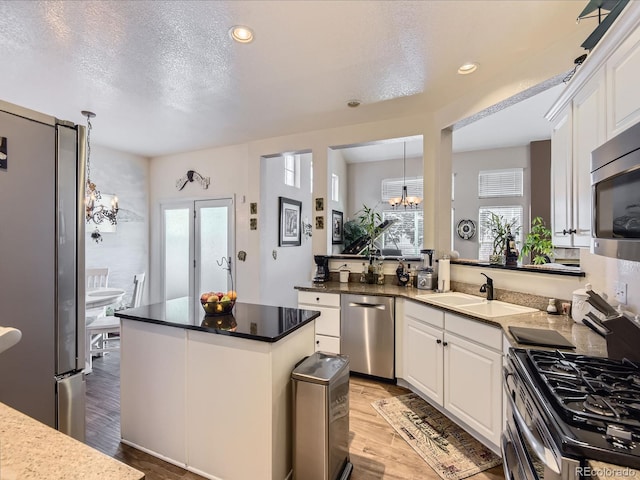 2676 S Troy Ct, Aurora, CO 80014 - kitchen with a kitchen island, a sink, light wood-style floors, appliances with stainless steel finishes, and an inviting chandelier