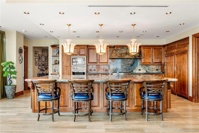 kitchen with a large island, tasteful backsplash, light stone counters, pendant lighting, and built in appliances