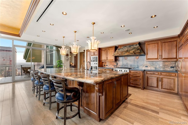 kitchen featuring dark stone counters, custom range hood, light hardwood / wood-style floors, tasteful backsplash, and a large island