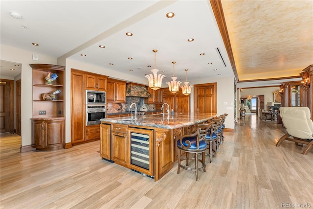 kitchen featuring appliances with stainless steel finishes, decorative light fixtures, light hardwood / wood-style floors, a spacious island, and beverage cooler