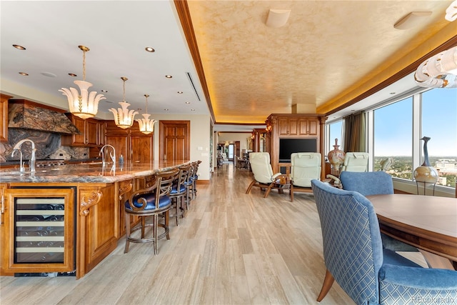 dining area with a raised ceiling, a chandelier, light wood-type flooring, and beverage cooler